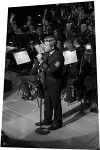 Sänger und Hornist Sebastian Römer am Mikrophon vor dem Orchester.