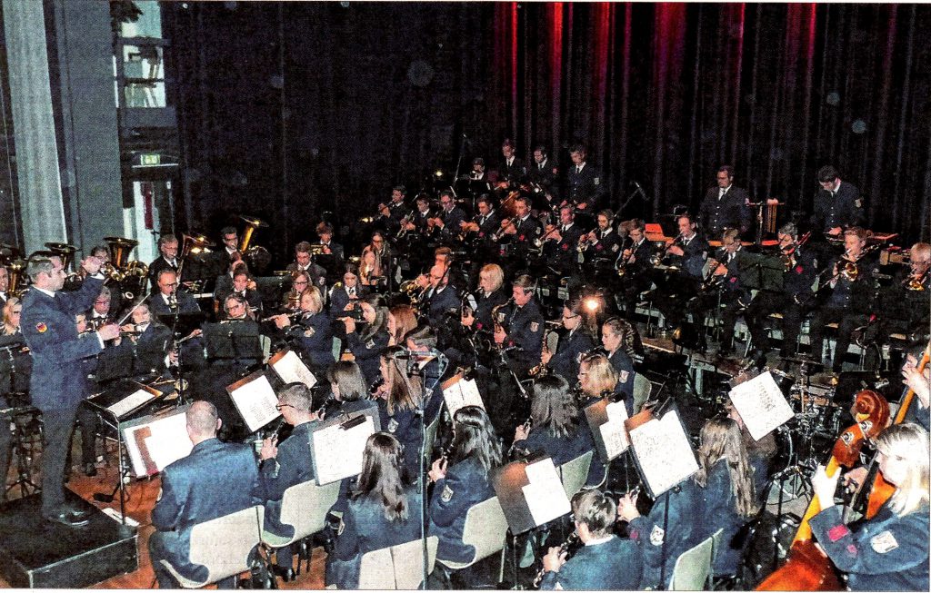 Foto des Orchesters. Andreas Reuber beim Dirigat, die Musikerinnen und Musiker im Spiel.